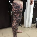 Фото тату на ноге с изображением японского самурая в доспехах, выполненное в черно-серых тонах с высокой детализацией и реалистичной проработкой.