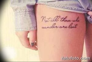 Фото тату надписи "Not all those who wander are lost" на бедре. Тонкий шрифт и минималистичный дизайн.