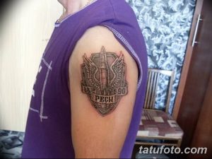 Фото тату на плече с изображением патрона в щите с крыльями и надписью 'ПЕЧ 88-90'. Реалистичный рисунок татуировки.