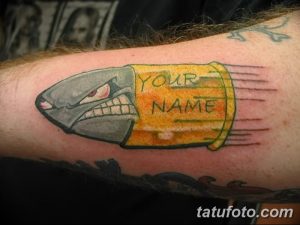 Фото татуировки гильзы от патрона с надписью 'YOUR NAME' в стиле олдскул. Яркий рисунок с использованием желтого, красного и черного цветов.