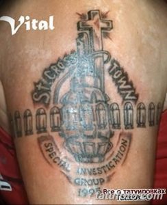 Фотография татуировки на руке, выполненной в темных тонах. Изображение включает в себя крест, оружие и надписи, создавая геральдический образ.