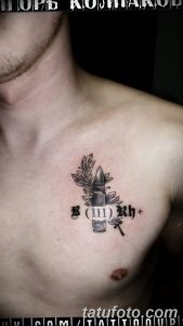 Фотография татуировки на груди с изображением патрона, обвитого веточкой. Детализированный рисунок в черно-белых тонах, символизирующий жизнь и защиту.