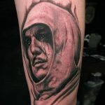 Фото тату на предплечье: реалистичный портрет мужчины в капюшоне с каплями дождя на лице. Черно-серые тона, детализированная проработка, драматичный эффект.