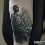 Фотография татуировки с изображением монаха, сидящего в позе медитации на фоне гор и тумана. Черно-серые тона, реалистичная проработка деталей.