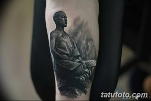 Фотография татуировки с изображением монаха, сидящего в позе медитации на фоне гор и тумана. Черно-серые тона, реалистичная проработка деталей.