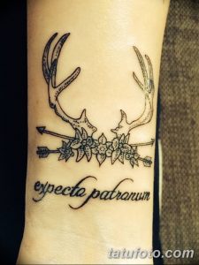 Фото тату оленьих рогов, цветов и надписи "expecto patronum" на предплечье. Черно-белый рисунок в стиле графика.