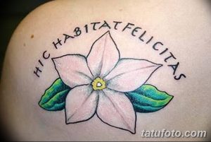 Фото тату цветка на плече. Розовый цветок с зелеными листьями и латинской надписью. Женский рисунок татуировки.