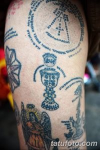 Фото тату рукава с множеством религиозных символов, включая чашу, кресты, надписи на разных языках. Черно-серый рисунок татуировки выглядит детализированным и сложным.