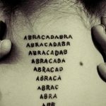 Фото тату с надписью 'Абракадабра', выполненной в виде уменьшающейся пирамиды на затылке мужчины. Черный рисунок татуировки выглядит минималистично и загадочно.