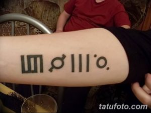 Фото тату на предплечье: минималистичный рисунок, состоящий из геометрических фигур и символов, выполненный черными чернилами, символизирующий личные убеждения.