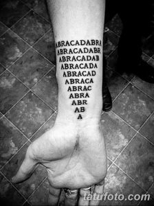 Фото тату на предплечье с текстом "Abracadabra", написанным в виде пирамиды. Слова уменьшаются в размере к низу. Рисунок выполнен в черном цвете.
