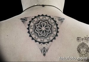 Фотография татуировки в славянском стиле на спине. Изображение круга с коловратом внутри и точечным орнаментом.