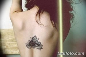 Фото тату на спине: Всевидящее око в треугольнике с надписями 'Realities' и 'Lies'. Черно-белый рисунок татуировки с четкими линиями.