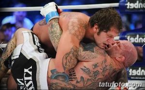 Фото татуировок на теле бойца MMA во время боя. Множество рисунков, покрывающих плечи, грудь и руки.