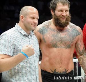 Фото тату на груди и руках бойца MMA: орнамент, религиозные символы, темные тона, реалистичный рисунок татуировки.