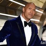 Фотография Дуэйна Джонсона в элегантном смокинге, на которой видна его татуировка на плече. Актер позирует на фоне футуристического интерьера.