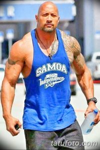 Фотография Двейна Джонсона в синей майке с надписью "SAMOA Independence Day" и татуировкой на руке. Мужчина держит бутылку воды.
