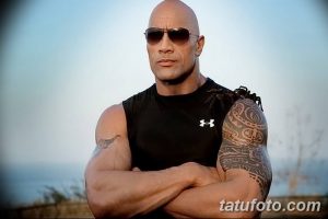 Фотография Двейна Джонсона в черной футболке и солнечных очках, демонстрирующая его татуировку на плече.