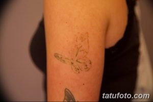 Фотография нечеткого рисунка татуировки бабочки на руке, выполненного тонкими линиями. Видны контуры крыльев и тела насекомого.