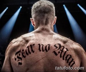 Фото татуировки на спине мужчины с надписью 'Fear no Man' выполненной готическим шрифтом. Черно-серая татуировка, символизирующая смелость и уверенность.