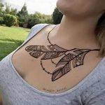 Фото тату: Небольшой черно-белый рисунок в стиле мехенди с изображением пера и точек на женской груди. Лаконичный и элегантный эскиз.