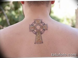 Фото татуировки кельтского креста на спине мужчины. Рисунок выполнен в приглушенных тонах с акцентом на детализацию узоров.