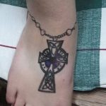 Фото тату кельтского креста на стопе с цепью. Черно-белый рисунок с детализированными узлами и переплетениями. Необычное и стильное расположение.