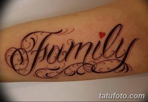 Фото татуировки с надписью 'Family' выполненной красивым шрифтом и украшенной маленьким красным сердцем. Расположена на предплечье.