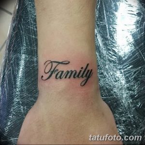 Черно-белое фото татуировки надписи 'Family' на запястье. Классический шрифт с завитушками, выполненный в черном цвете. Изящный и стильный дизайн.