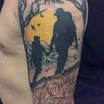 Фото тату на предплечье с изображением отца и дочери на фоне заката и деревьев. Черно-серый рисунок татуировки символизирует любовь и защиту.
