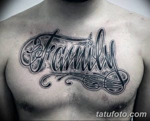 Фото тату: большая и сложная татуировка надпись "Family" с декоративными элементами и завитушками на груди. Татуировка выполнена в черно-серых тонах.