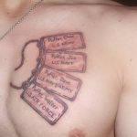 Фото тату на груди, изображающее цепочку из жетонов с именами военнослужащих. Серые тона, реалистичный стиль.