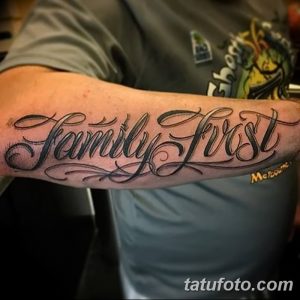 Фото татуировки на предплечье с надписью 'Family First', выполненной красивым каллиграфическим шрифтом. Черно-серый рисунок с декоративными элементами.