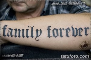 Фото татуировки на предплечье с надписью 'Family Forever', выполненной готическим шрифтом. Черно-белый рисунок с небольшим символом на запястье.
