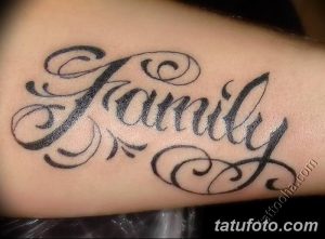 Фото тату на руке с надписью 'Family' выполненной красивым шрифтом и украшенной витиеватыми узорами. Черно-серая татуировка.