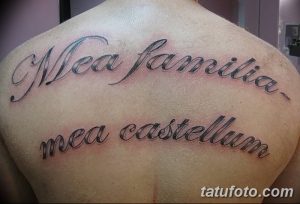 Фото тату на спине с латинской надписью 'Mea familia, mea castellum' выполненной каллиграфическим шрифтом. Черно-серая татуировка.