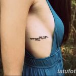 Фото татуировки с изящной надписью, выполненной каллиграфическим шрифтом, на женском боку. Тату выглядит нежно и элегантно.