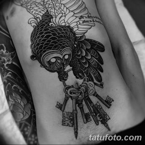 Фото тату на боку: ворон с ключами в лапах, выполненное в стиле blackwork с использованием черного цвета и точечной штриховки.