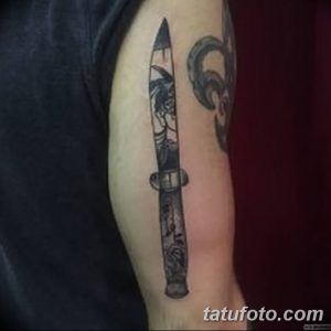 Черно-белое фото тату складного ножа на плече, с детальной проработкой лезвия и рукояти, выполненное в реалистичном стиле.