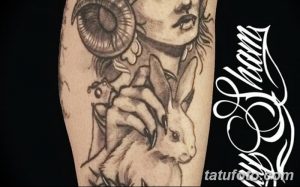 Фото татуировки на руке с изображением женщины с рогами, держащей кролика. Рисунок выполнен в черно-серых тонах с детальной проработкой.