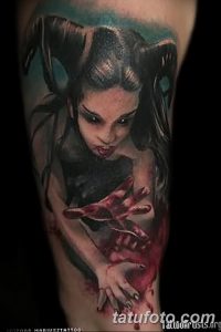 Фото тату с изображением вампирши с рогами и красными глазами на руке. Реалистичный рисунок с темным фоном и кровавыми брызгами.