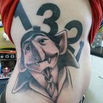 Фото тату на боку с изображением персонажа в шляпе и цифрами 13 и 2. Рисунок выполнен в черно-белой гамме.