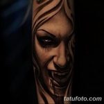 Фото тату улыбающейся вампирши на руке. Черно-белый рисунок татуировки с острыми клыками и безумным взглядом.