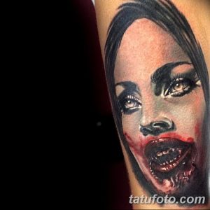 Фото тату на руке с изображением вампирши с кровавым оскалом и пронзительным взглядом, выполненное в реалистичном стиле с использованием красных и черных оттенков.