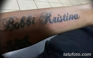Фото татуировки с надписью "Bobbi Kristina", выполненной каллиграфическим шрифтом, на предплечье руки. Черно-серый рисунок татуировки.