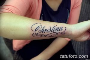 Фото тату надписи 'Christina' на запястье. Черно-серая татуировка, выполненная изящным шрифтом с декоративными элементами, выглядит женственно и стильно.