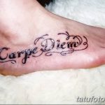 Фото тату надписи 'Carpe Diem' с декоративными завитушками и узорами, выполненной на верхней части стопы.