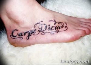 Фото тату надписи 'Carpe Diem' с декоративными завитушками и узорами, выполненной на верхней части стопы.