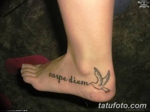 Фото тату надписи 'Carpe Diem' и изображения голубя на лодыжке девушки. Татуировка выполнена в черно-белой гамме.