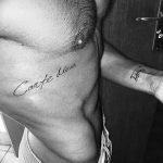 Фото тату надписи 'Carpe Diem' черным цветом на груди и предплечье мужчины. Дополнительно на руке изображена небольшая татуировка.